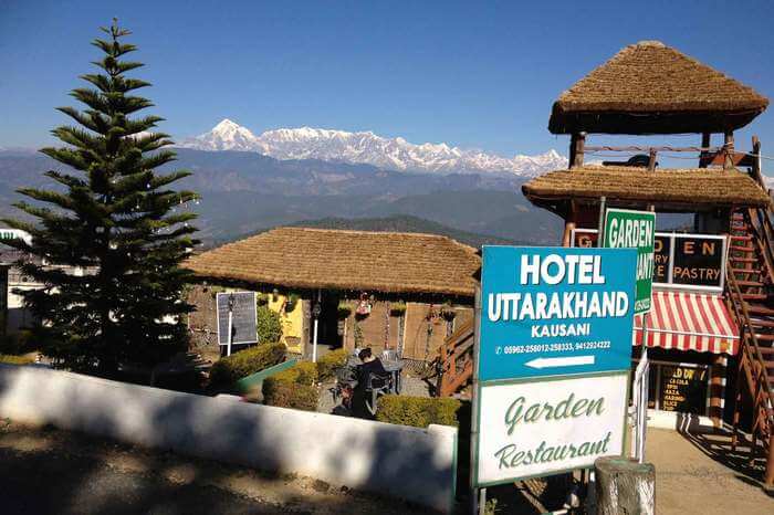 Thatched roof restaurant with a board in front and snow laden mountains in the back