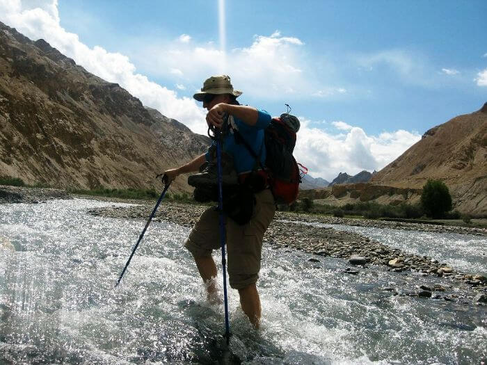 A trekker crosses a river during the ripchar valley trek