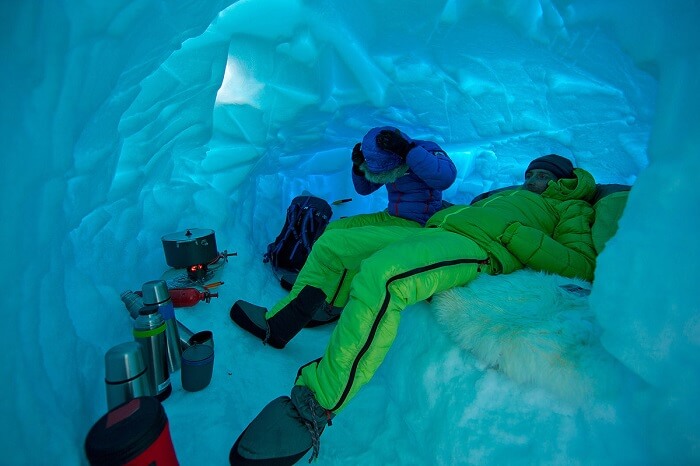 Two men cooking and relaxing while snow cave camping