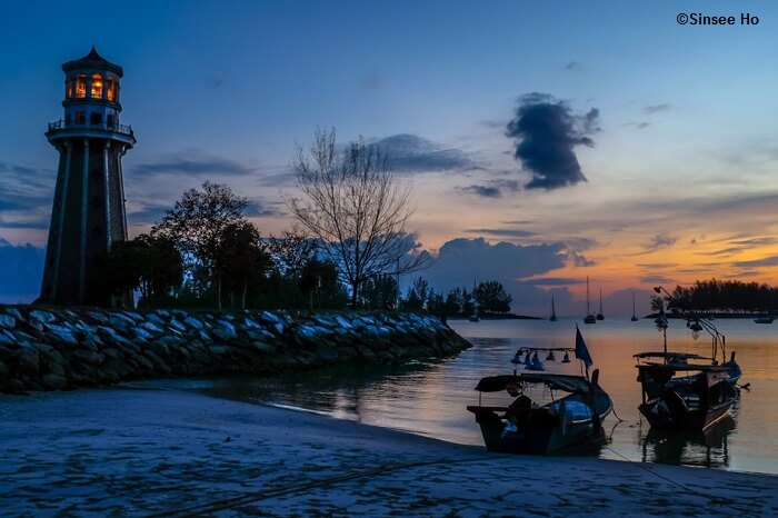Boats dock at the Pantai Kok beach near the grand lighthouse as the sun sets into the sea