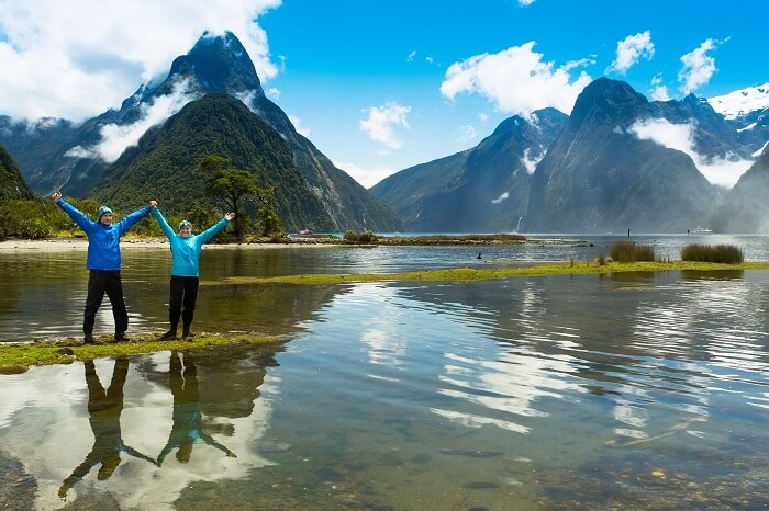 Happy couple on the beach near the waterfall at Milford Sound on South Island of New Zealand