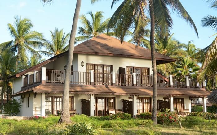 an open pool surrounded by palm trees in a Zanzibari thatched roof resort