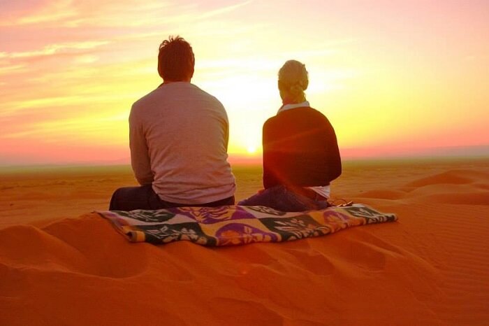 A couple enjoying a beautiful sunset in the Sahara Desert on their Morocco honeymoon