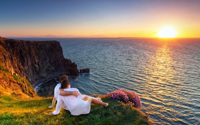 Couple relaxing on a cliff savoring the sunrise view in Ireland