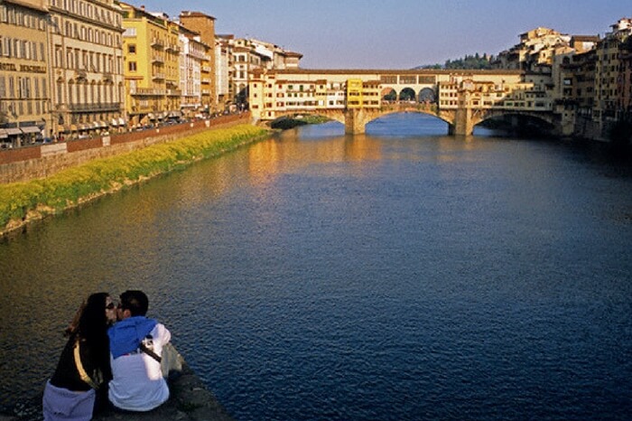 Couple kissing on the bank of a river in Siena