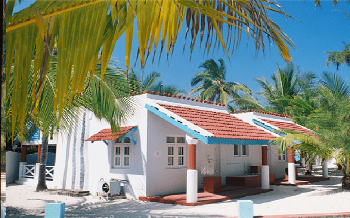 A beach resort painted white and blue surrounded by palm trees