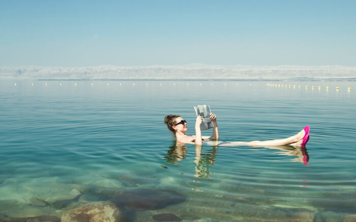 A woman reading newspaper while floating on the waters of Dead Sea
