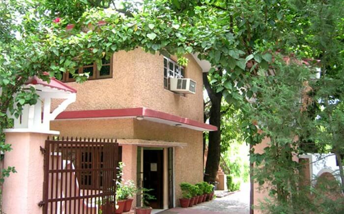 Entry of a hotel covered by green trees and creepers