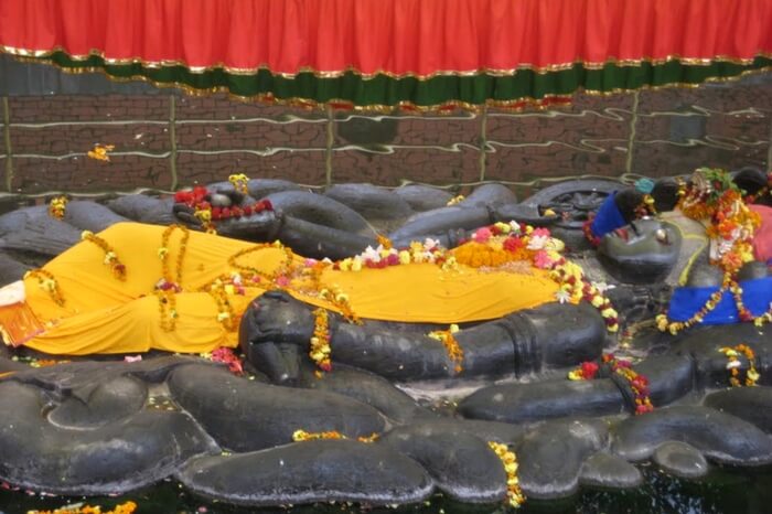 A black stone statue of a god wearing flowers and a yellow sheet