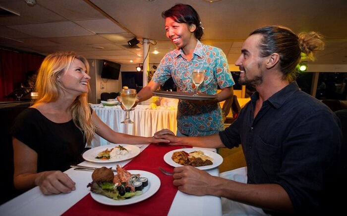 young couple eating food on a cruise while a lady serves