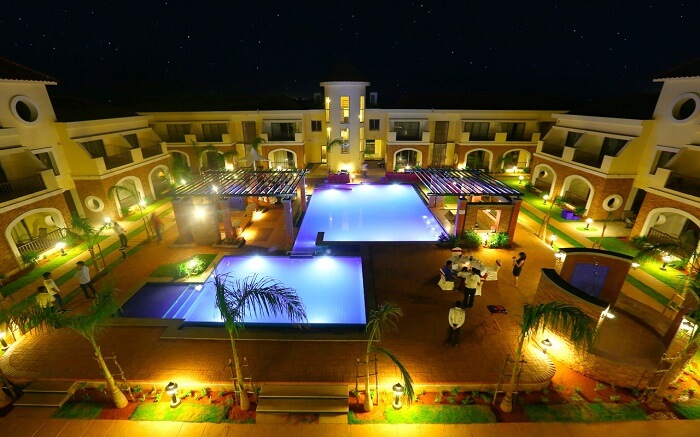 Two outdoor pools and a well lit lawn of a hotel
