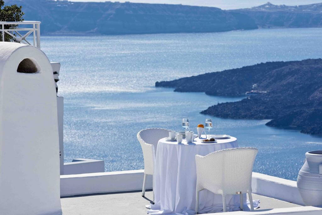 white table and chairs on a terrace overlooking caldera